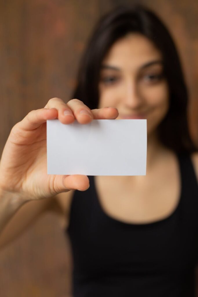 Soft focus of positive ethnic female in casual wear looking at camera while demonstrating white mock up business card in hand